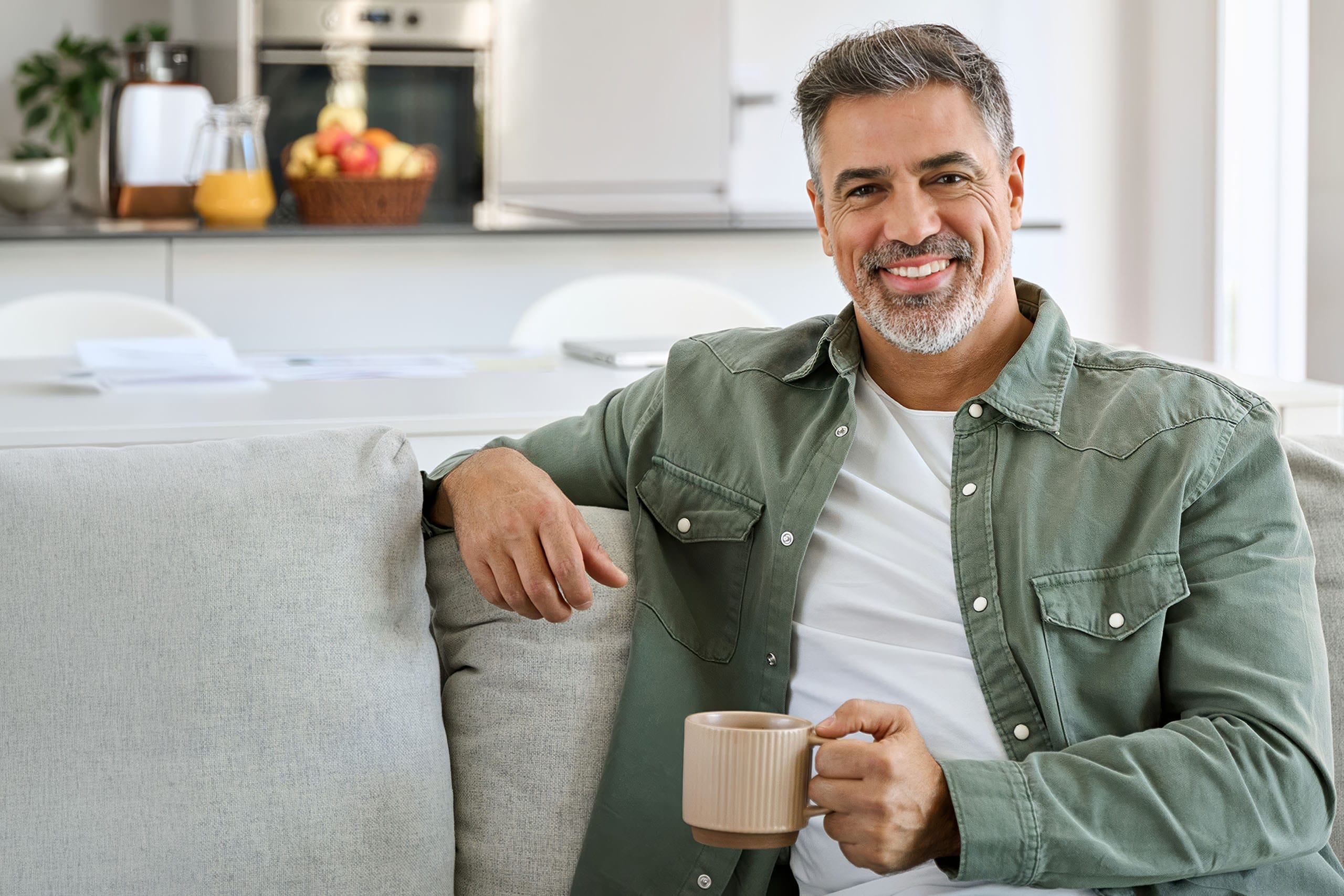 Smiling middle-aged man relaxing on a couch at home while holding a coffee mug