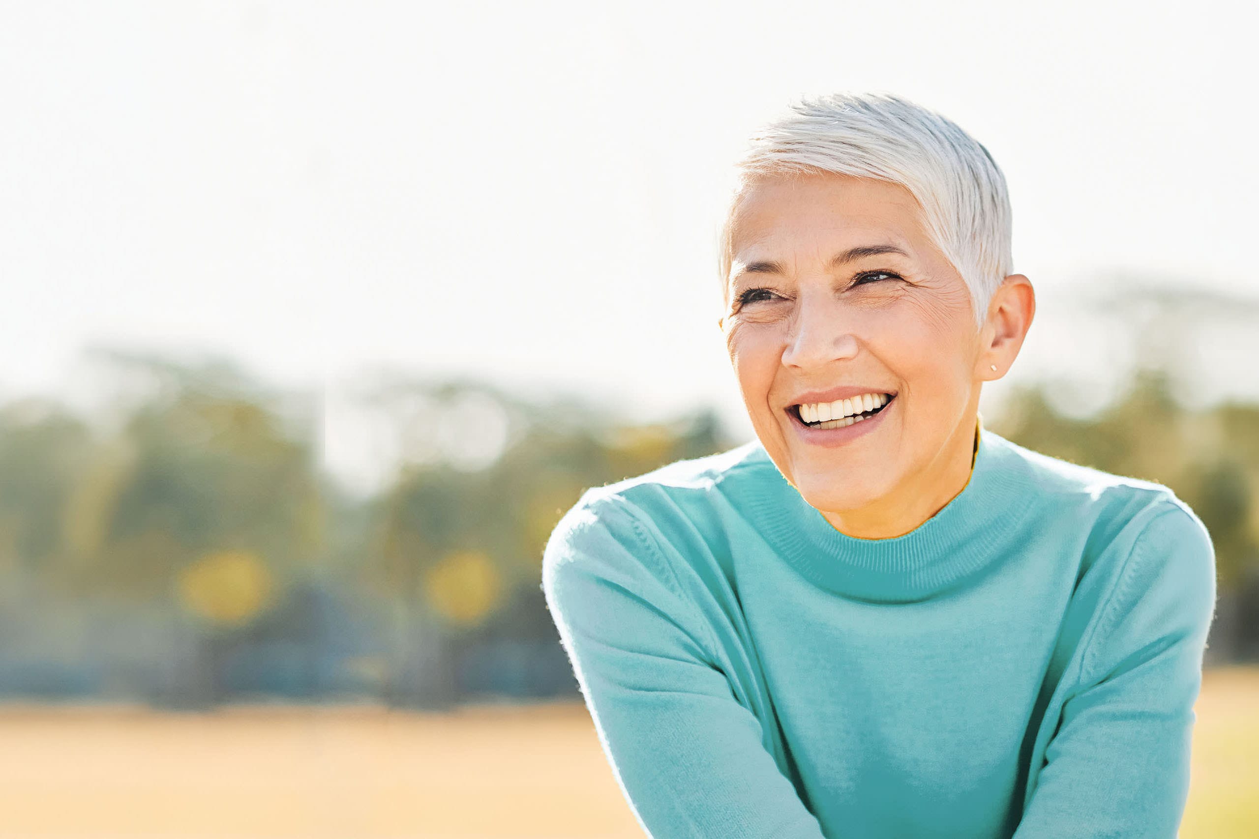 Smiling older woman with short gray hair enjoying a sunny day outdoors.