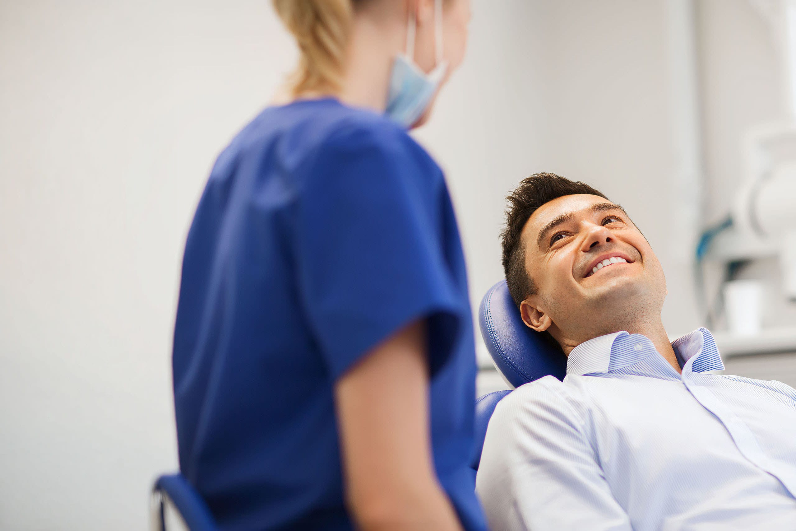Male patient smiling in a dental chair while speaking with a dental professional in a clinic